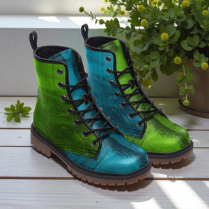 A pair of vibrant green and blue boots with black laces, placed on a wooden surface next to a potted plant.
