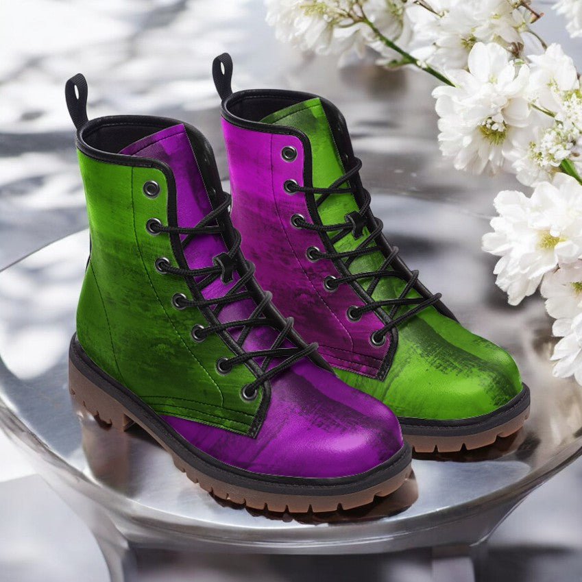 A pair of colorful, patterned boots with green and purple hues, placed on a reflective surface with white flowers in the background.