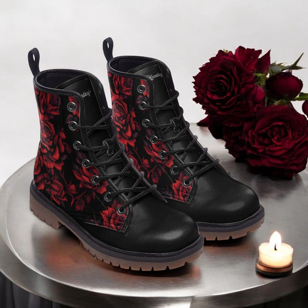 A pair of black boots with red rose designs, placed on a round table next to a lit candle and a bouquet of red roses.