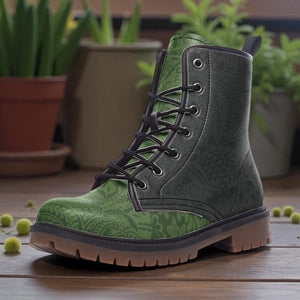 A pair of green patterned boots with black laces, placed on a wooden surface with potted plants in the background.