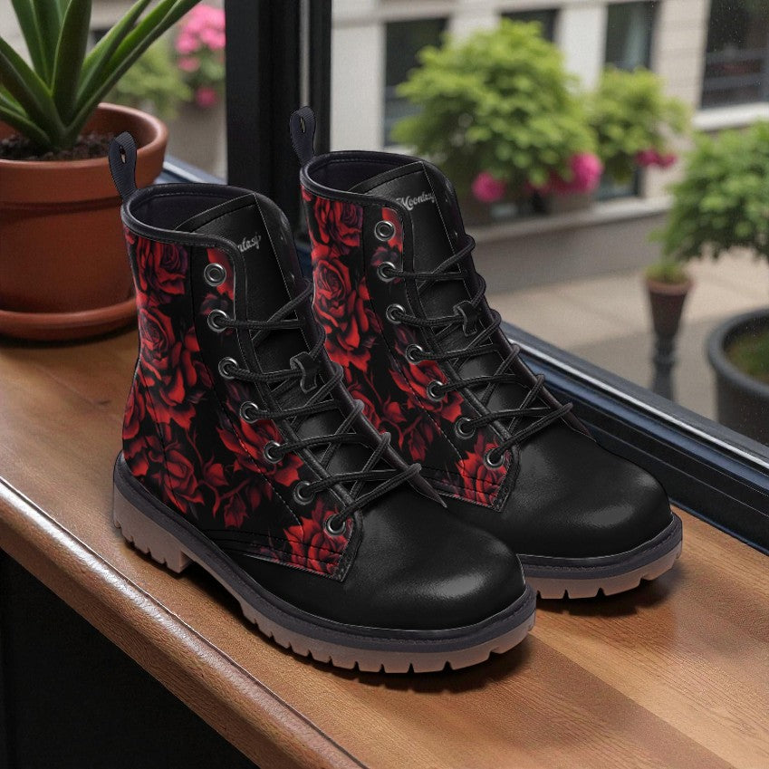 A pair of black boots with red floral patterns, placed on a wooden surface near a window with potted plants visible outside.