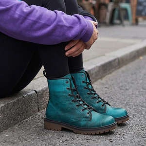 A person wearing a purple hoodie and blue boots is sitting on a curb, with their legs crossed.