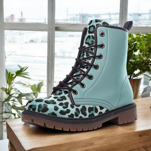 A blue and black leopard print boot is displayed on a wooden surface, with a window and plants visible in the background.