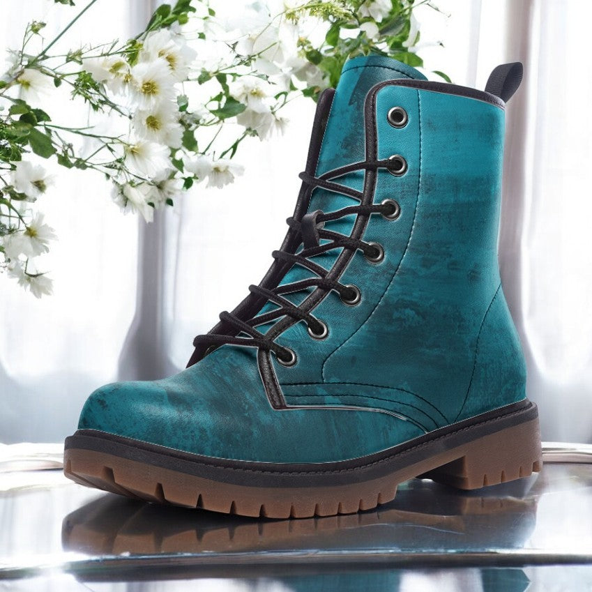 A teal-colored boot with a lace-up design is displayed against a backdrop of white flowers and a window.
