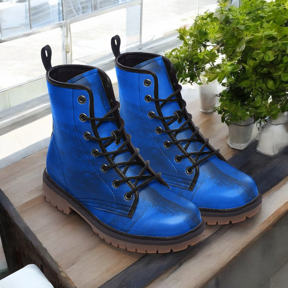 A pair of blue combat boots with black laces and soles, placed on a wooden surface near a window with potted plants.