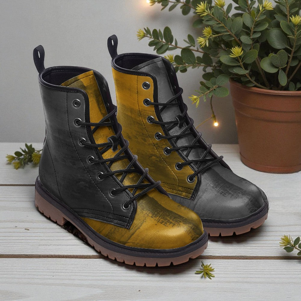 A pair of black and yellow boots with laces and soles, placed on a wooden surface next to a potted plant.