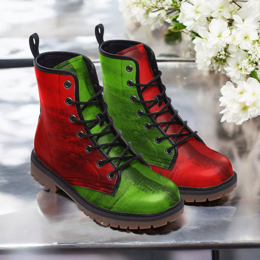 A pair of vibrant red and green combat boots are displayed on a reflective surface, with white flowers in the background.