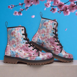 A pair of pink floral printed boots stands against a blue background with cherry blossom flowers in the background.