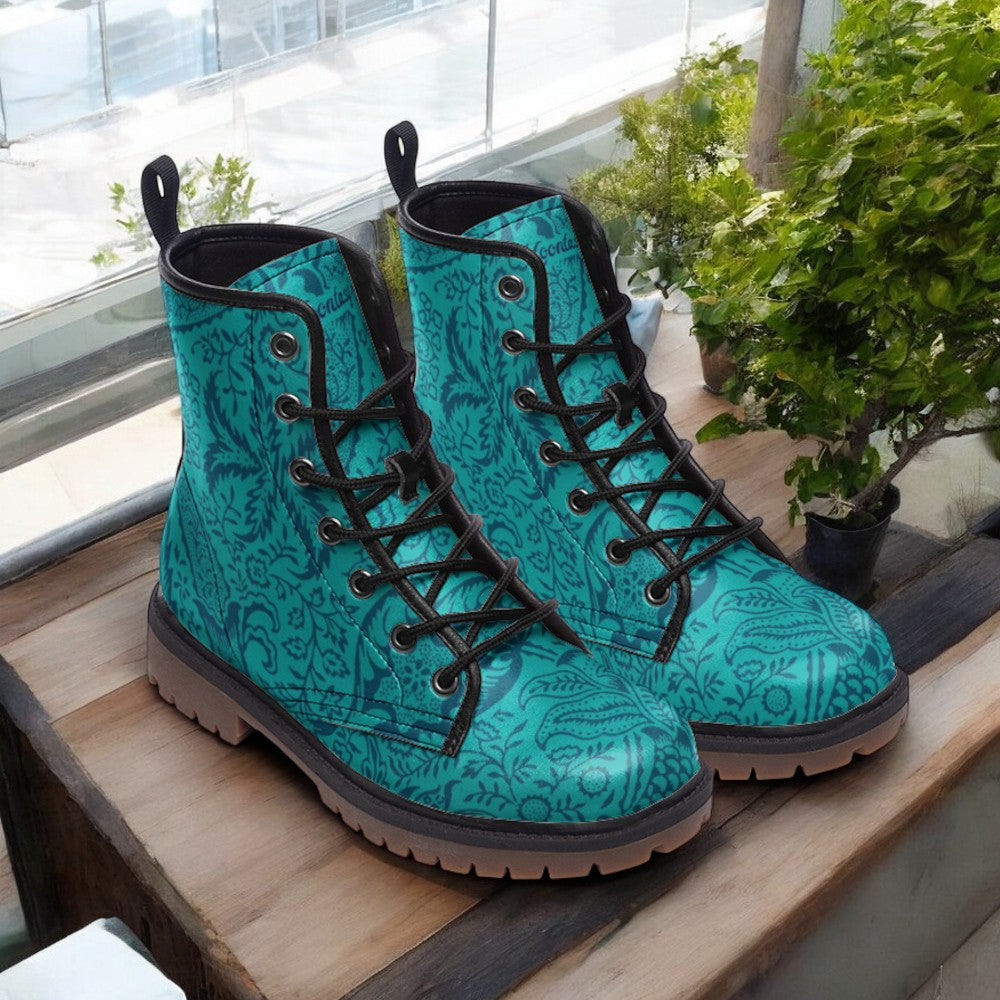 A pair of teal patterned boots with black laces, placed on a wooden surface next to a potted plant.