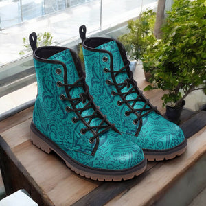 A pair of teal patterned boots with black laces, placed on a wooden surface next to a potted plant.