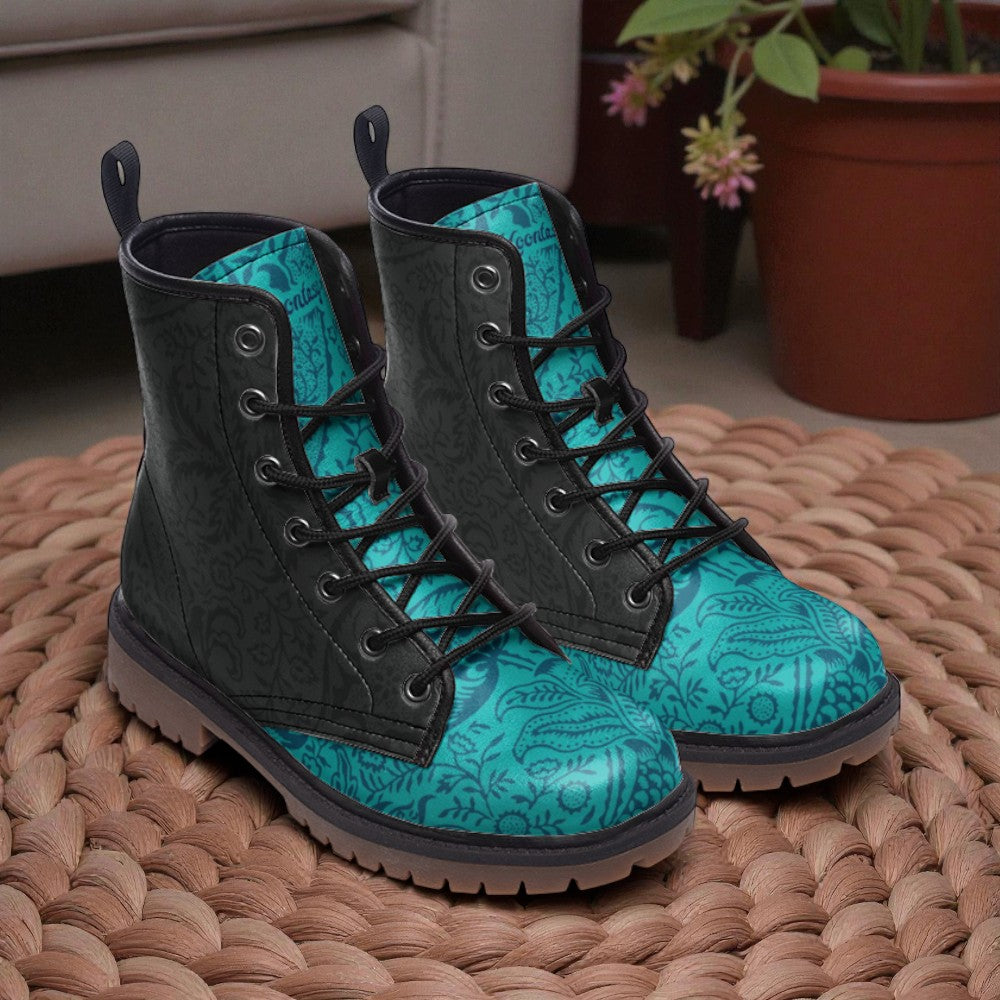 A pair of teal and black patterned boots with laces and soles, placed on a woven mat.