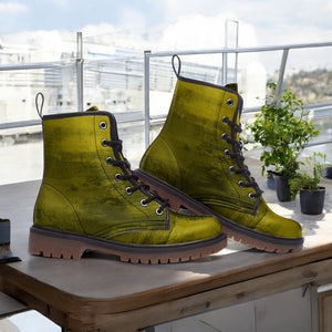 A pair of green combat boots with a textured appearance, placed on a wooden surface near a window overlooking a cityscape.