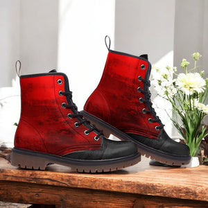 A pair of red and black combat boots with a distressed appearance, placed on a wooden surface next to a vase of white flowers.