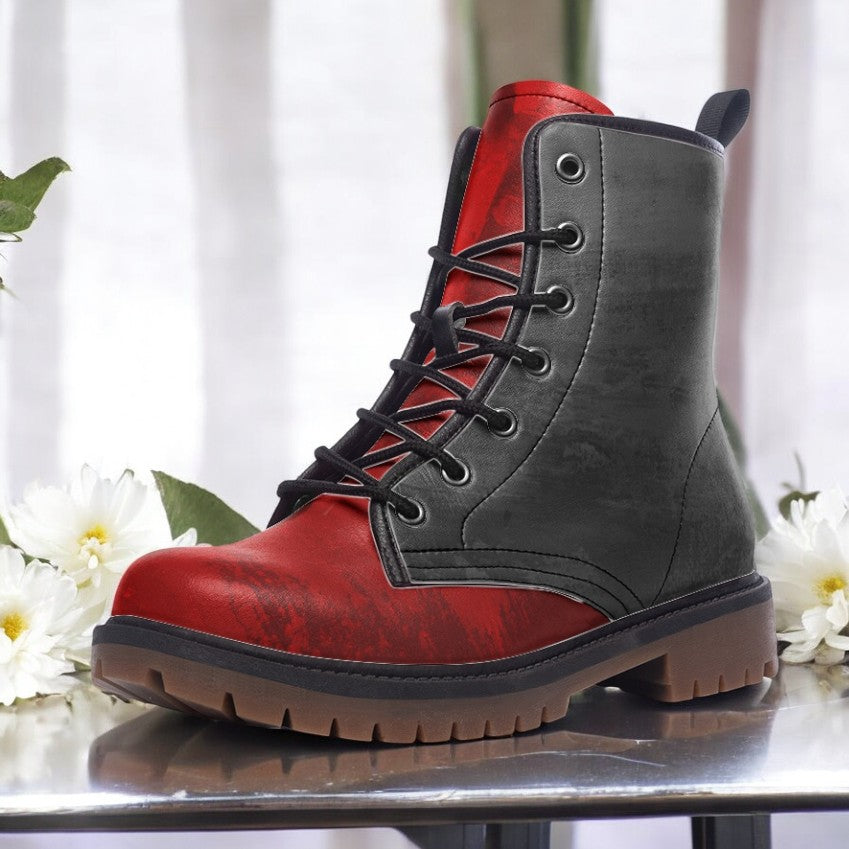 A red and black combat boot with a lace-up design and a rugged sole, placed on a reflective surface with white flowers in the background.