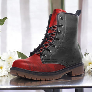 A red and black combat boot with a lace-up design and a rugged sole, placed on a reflective surface with white flowers in the background.