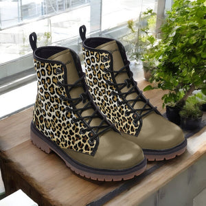 A pair of leopard print boots sits on a wooden surface, with a potted plant visible in the background.