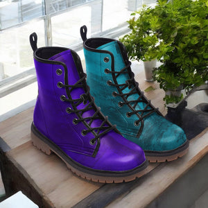 A pair of purple and blue combat boots are displayed on a wooden surface, with a potted plant visible in the background.
