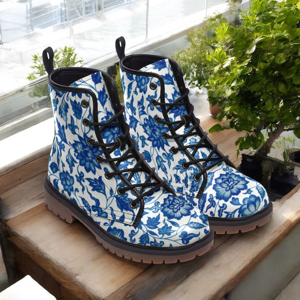 A pair of blue and white floral patterned boots are displayed on a wooden surface, with a potted plant visible in the background.