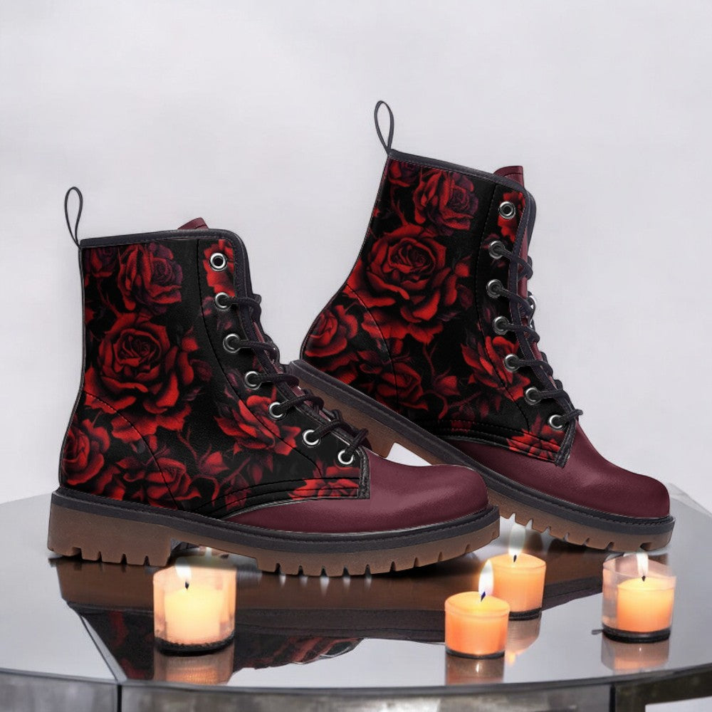 A pair of burgundy boots with a red rose pattern, placed on a reflective surface with three lit candles in front of them.