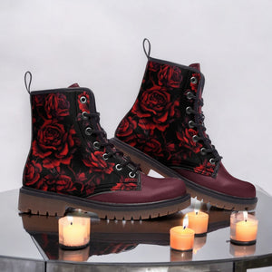 A pair of burgundy boots with a red rose pattern, placed on a reflective surface with three lit candles in front of them.