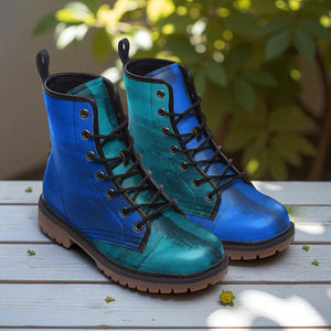 A pair of blue and green boots with black laces, placed on a wooden surface with some small yellow flowers around them.