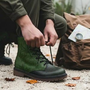 A person is tying the laces of a green and black patterned boot, with a brown backpack and a map visible in the background.
