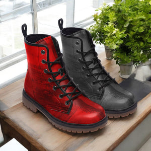A pair of red and black combat boots are displayed on a wooden surface, with a potted plant visible in the background.