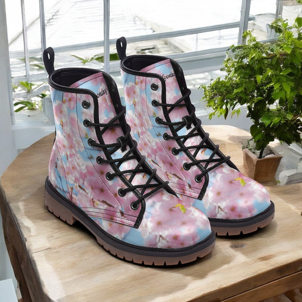 A pair of colorful floral-patterned boots with black laces, placed on a wooden surface near a window with greenery outside.