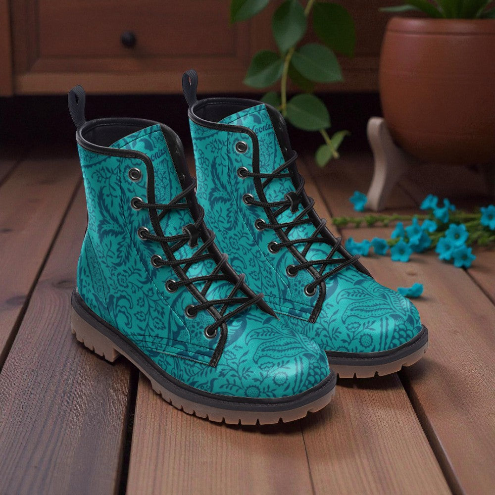 A pair of turquoise patterned boots with black laces, placed on a wooden surface with a potted plant and blue flowers in the background.