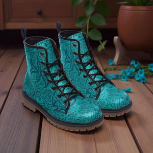A pair of turquoise patterned boots with black laces, placed on a wooden surface with a potted plant and blue flowers in the background.