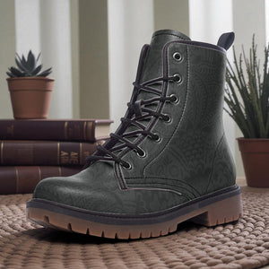 A pair of gray patterned boots sits on a woven mat, with a stack of books and potted plants in the background.