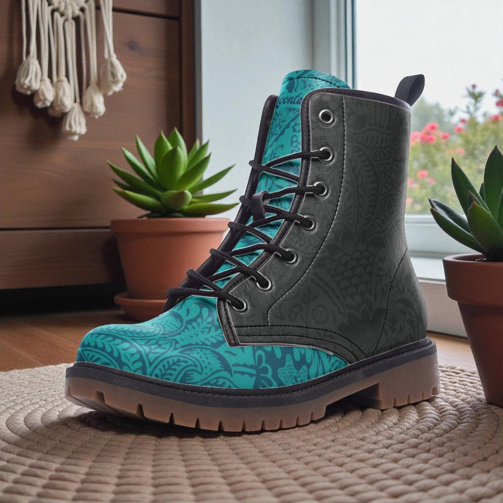 A pair of teal and black patterned boots sits on a woven mat, with potted plants and a wooden wall in the background.