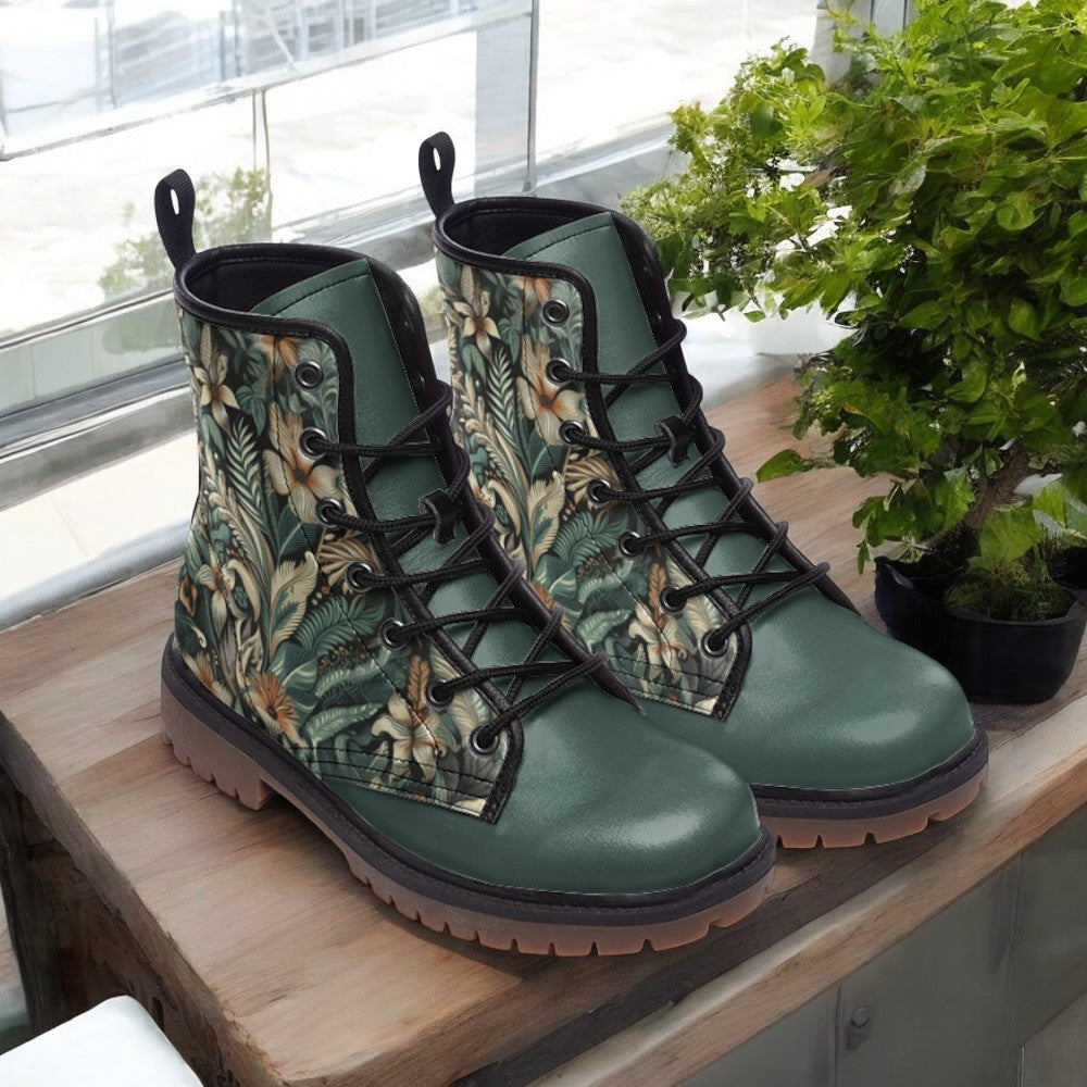 A pair of green floral patterned boots sits on a wooden surface, with a potted plant to the right.