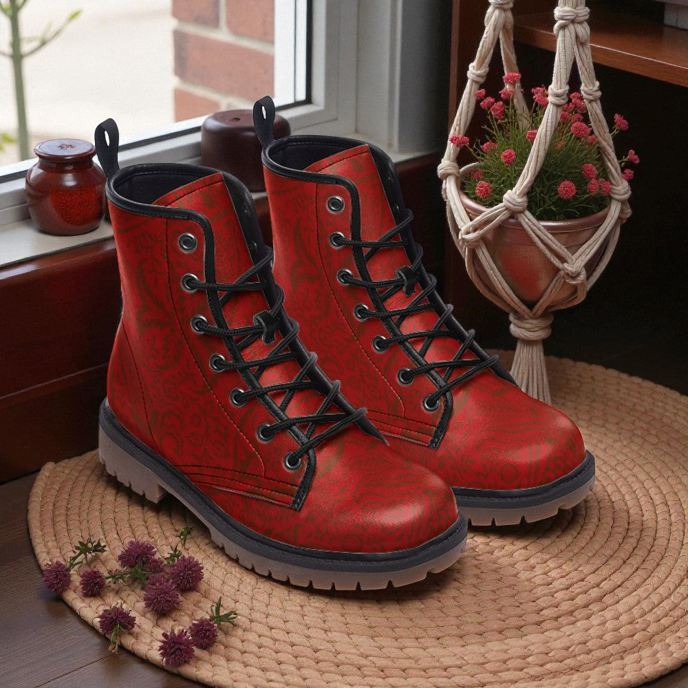 A pair of red patterned boots sits on a woven mat next to a window with a hanging plant and a small red pot.