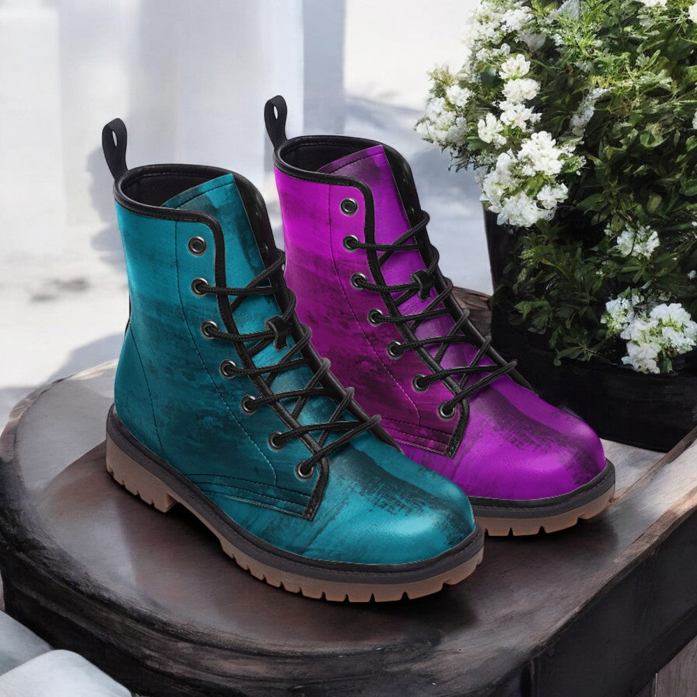 A pair of colorful boots, one in teal and the other in purple, are displayed on a wooden surface next to a potted plant with white flowers.