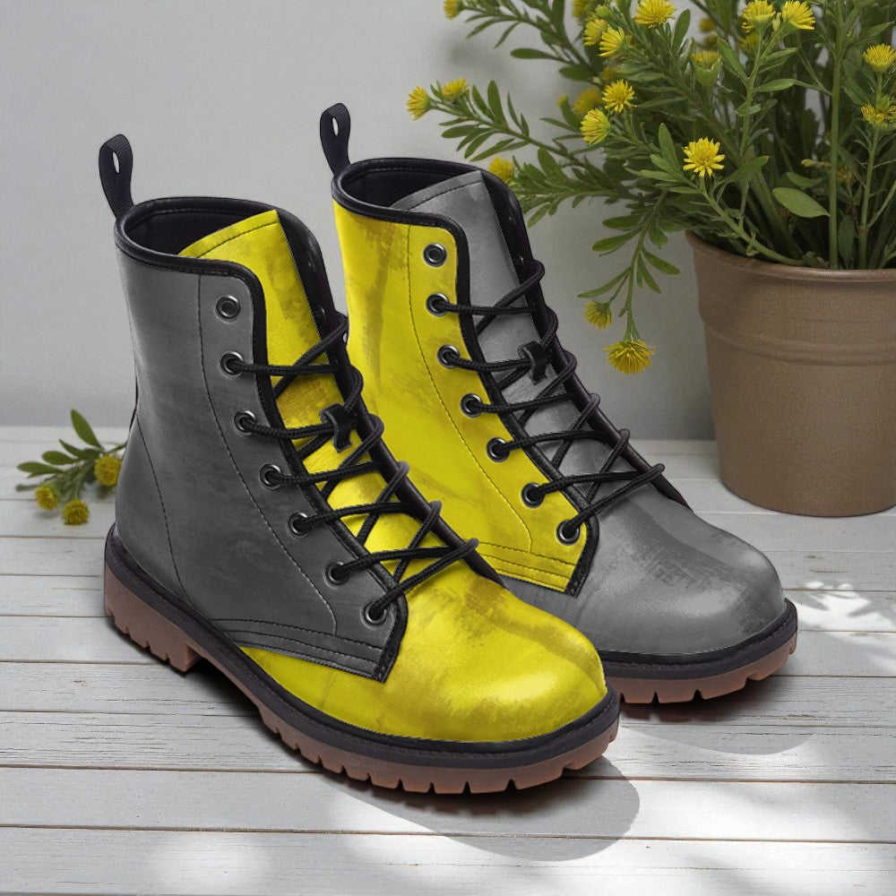 A pair of yellow and gray boots with black laces, placed on a wooden surface next to a potted plant with yellow flowers.
