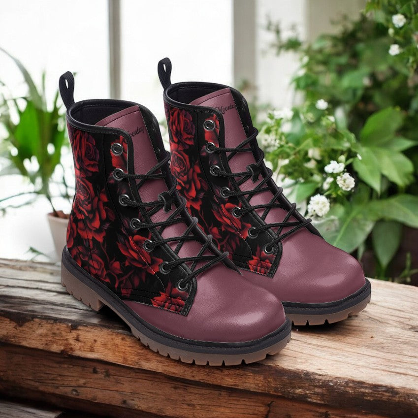 A pair of red and black floral patterned boots are displayed on a wooden surface, with a backdrop of greenery.