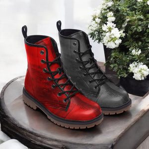 A pair of red and black combat boots are displayed on a wooden surface, with a potted plant and white flowers in the background.