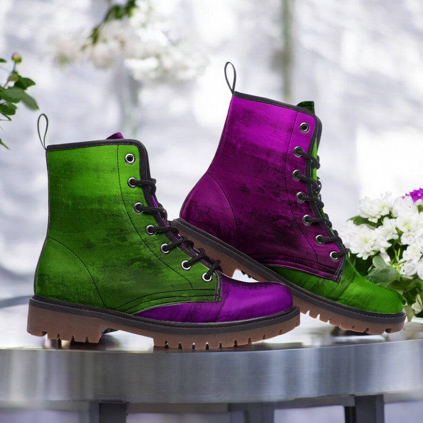 A pair of green and purple combat boots are displayed on a table, with white flowers in the background.