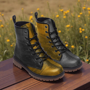 A pair of black and yellow boots with laces and soles, placed on a wooden surface against a background of yellow flowers.