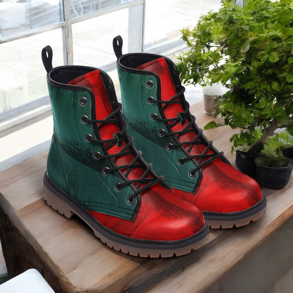 A pair of green and red combat boots are displayed on a wooden surface, with a potted plant in the background.