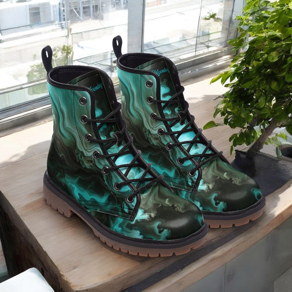 A pair of teal-colored, patterned boots with black laces and soles, placed on a wooden surface near a window.