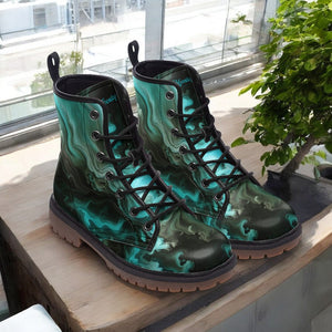 A pair of teal-colored, patterned boots with black laces and soles, placed on a wooden surface near a window.