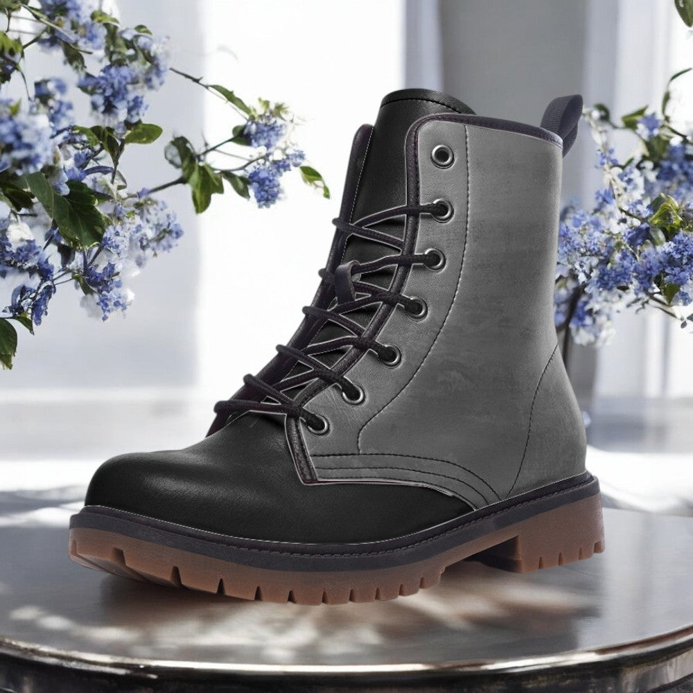 A black and gray leather boot with a rugged sole and lace-up closure, placed on a round metal surface.