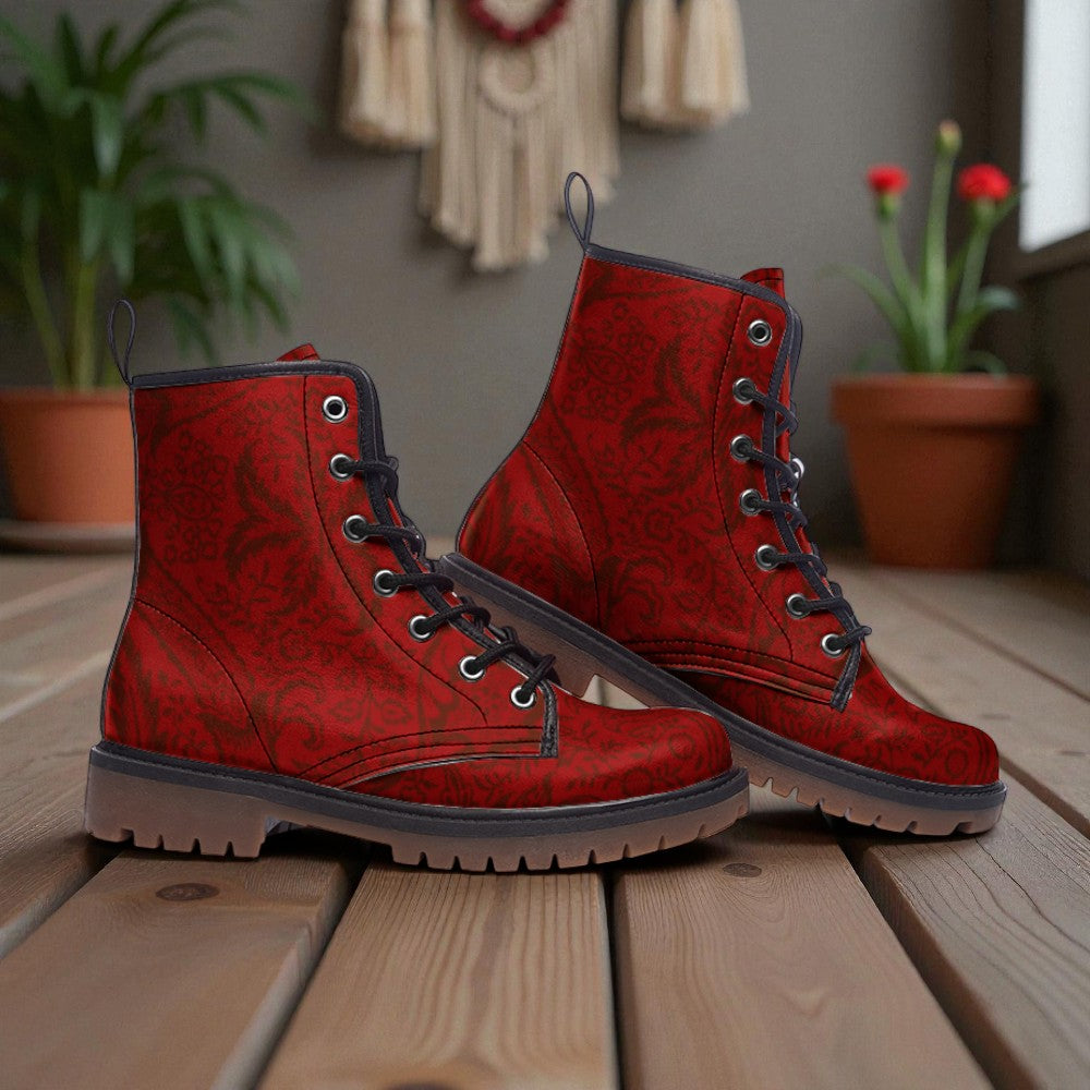 A pair of red patterned boots with black laces and soles, placed on a wooden surface with potted plants in the background.
