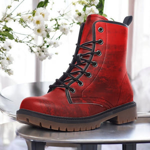 A red, textured, and patterned boot is displayed on a table, with white flowers visible in the background.