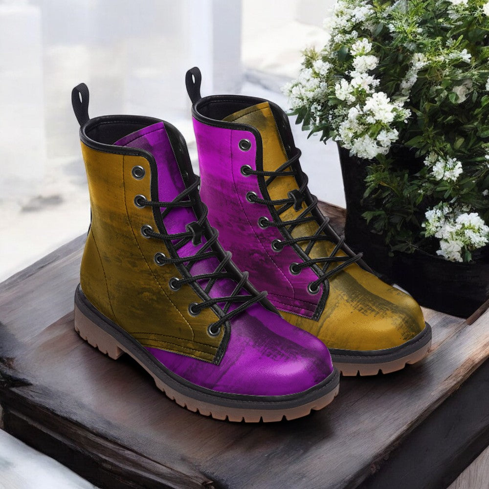 A pair of colorful, patterned boots with purple and yellow hues, placed on a wooden surface next to a potted plant with white flowers.