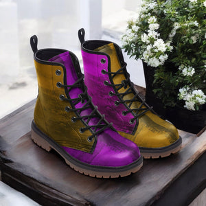 A pair of colorful, patterned boots with purple and yellow hues, placed on a wooden surface next to a potted plant with white flowers.