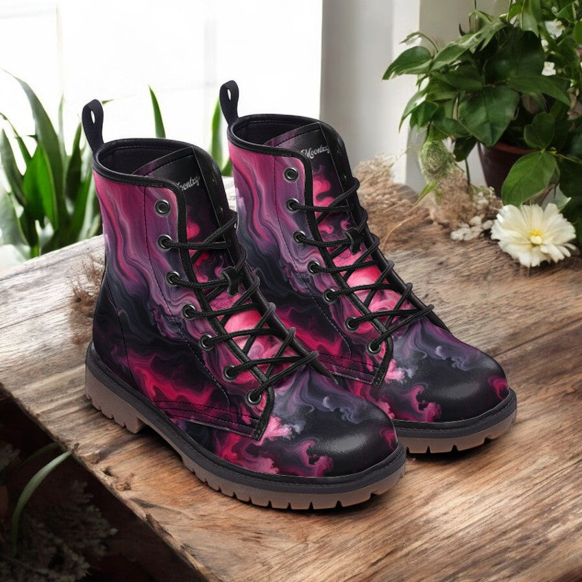A pair of vibrant, patterned boots with a mix of pink, purple, and black colors, placed on a wooden surface near a potted plant.