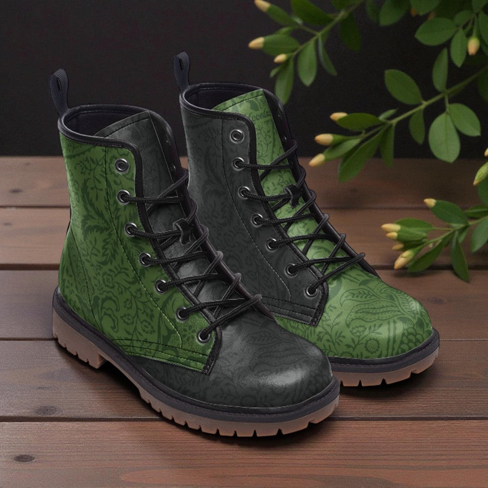 A pair of green patterned boots with black laces and soles, placed on a wooden surface with green leaves in the background.